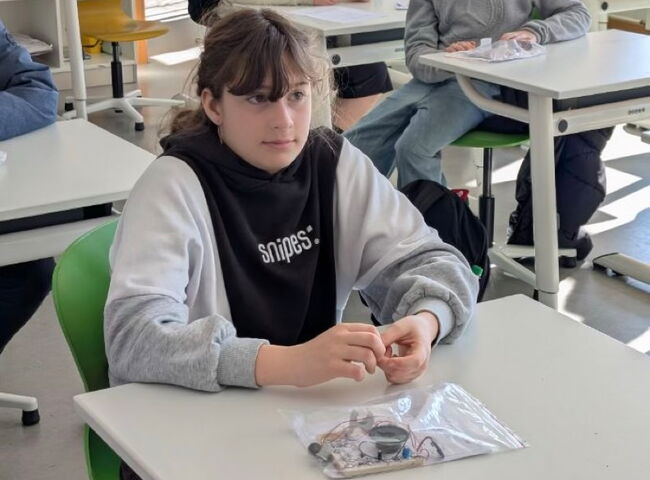 Schüler sitzen an Bänken und haben Tüten mit Elektronik vor sich