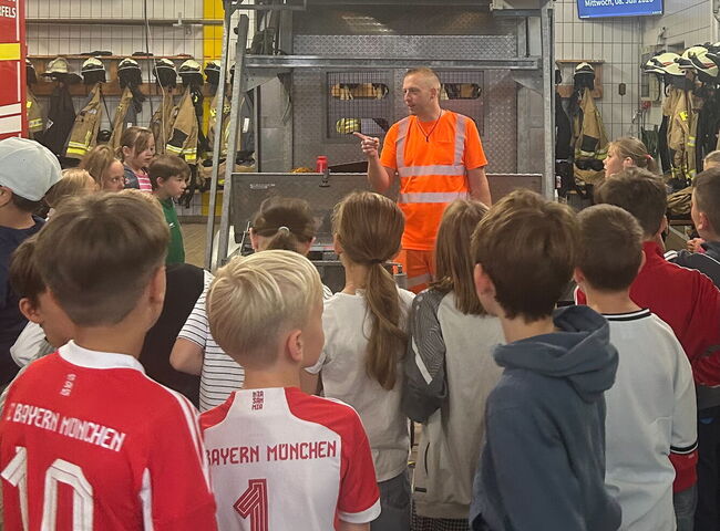 Ein Feuerwehrmann spricht mit Kindern im Gerätehaus