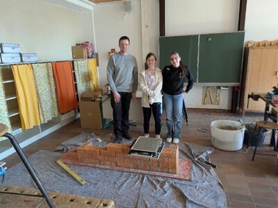 Zwei Schülerinnen stehen mit dem Ausbilder hinter einer kleinen gemauerten Ziegelwand